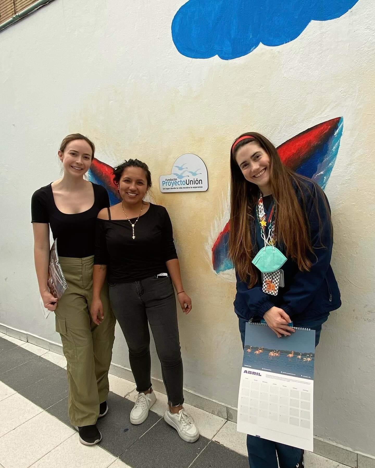 Tres mujeres frente a un mural de alas